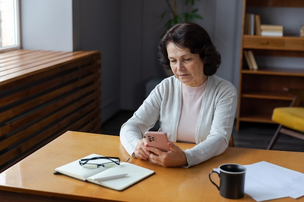 Europäische Seniorin mittleren Alters, die mit Smartphone-Touchscreen-Eingabe-Scroll-Seite stilvoll o