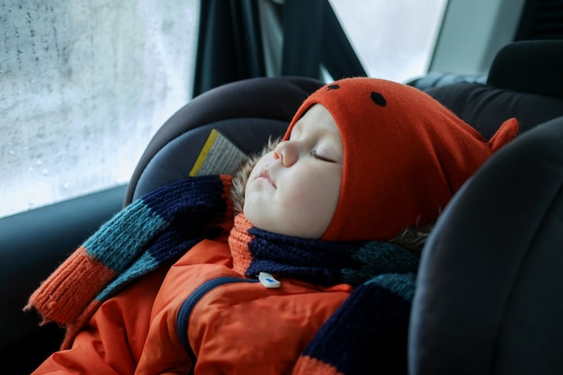 Europäischer Junge, der im Winter in Kleidern im Autositz im Auto schläft