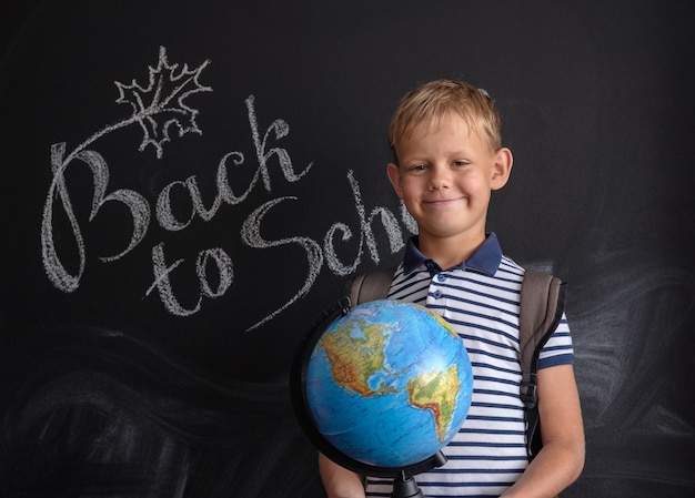 Europäischer Junge mit physischem Globus auf schwarzer Schulbehörde mit Inschrift zurück zur Schule