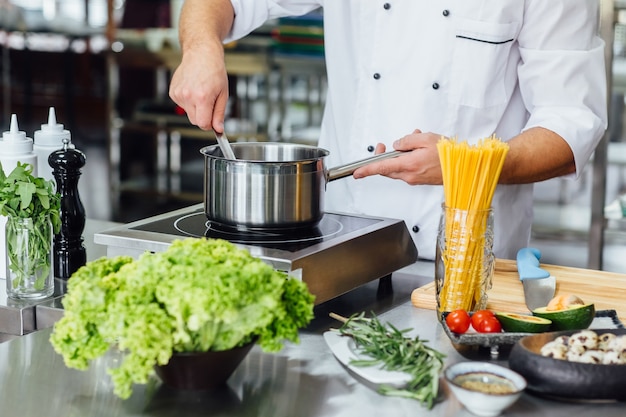 europäischer mann chef in weißer uniform kochteigwaren im topf in der küche im restaurant.