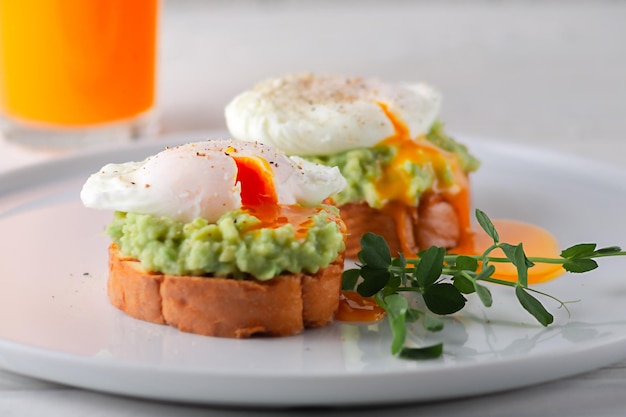 Europäisches Frühstück, geröstetes Brot mit pochiertem Avocado-Ei und Fruchtsaft auf einem weißen Holztisch, gesunde Ernährung
