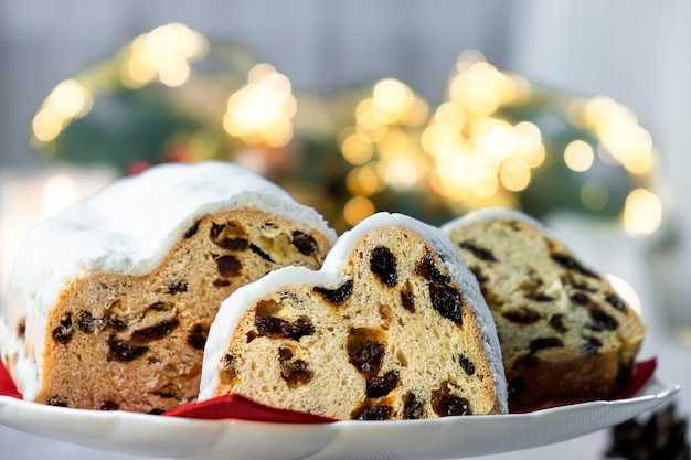 Europäisches Gebäckdessert mit Rosinen, Nüssen, Trockenfrüchten und Puderzucker, deutscher Stollenkuchen und warmer Weihnachtsbeleuchtung, magische Weihnachtsstimmung, fröhliche Weihnachten und ein gutes neues Jahr