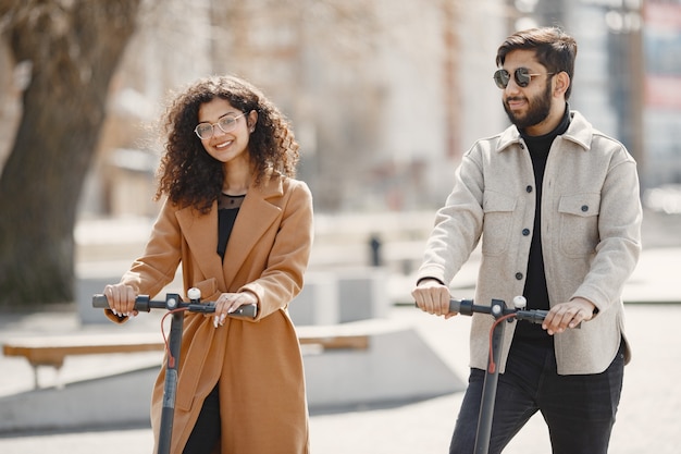 Europäisches Mädchen anindian Kerl fahren Roller und lächeln.