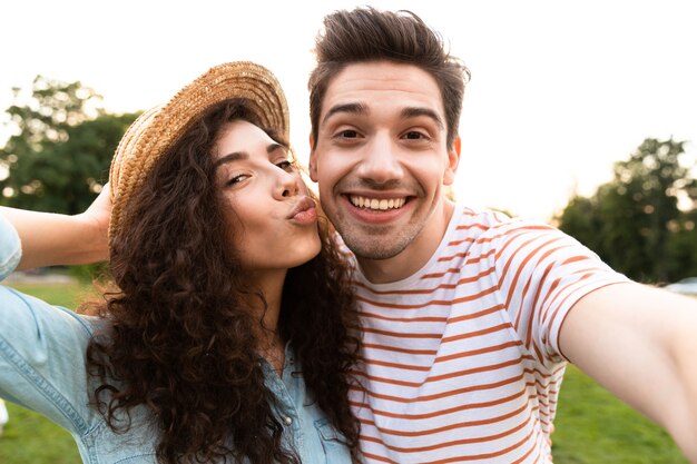Europäisches Paar, das im grünen Park geht und Selfie auf Handy nimmt