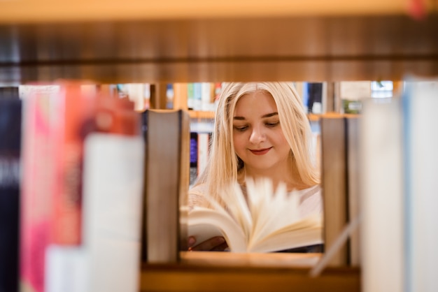Europäisches Studentenmädchen, das durch verschiedene Bücher schaut