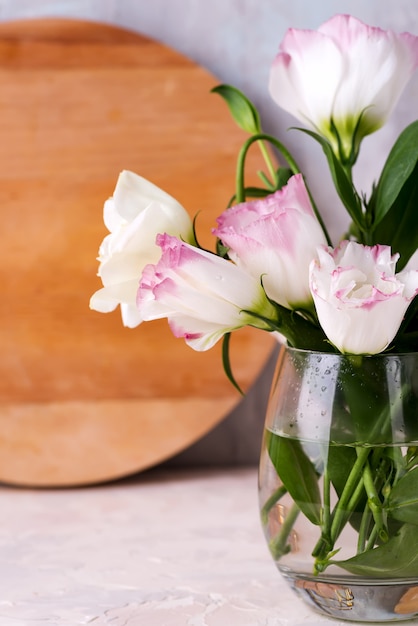 Eustoma blüht im Vase auf Tabelle nahe hölzerner Platte und Steinwand, Nahaufnahme.