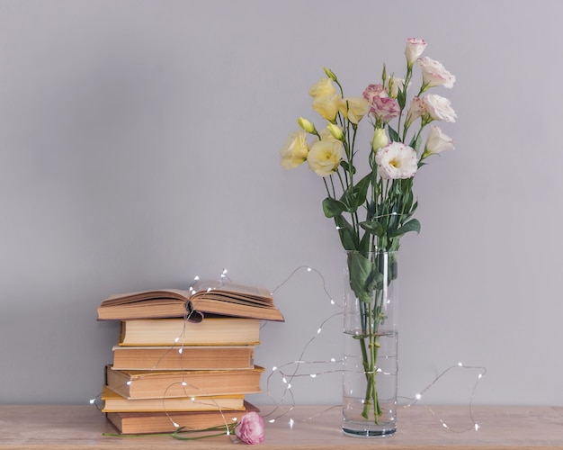 Eustoma buquê de flores em um vaso, pilha de livros antigos e luzes de guirlanda. Ler e relaxar o conceito.