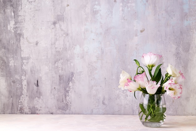 Eustoma floresce no vaso na mesa perto da parede de pedra, espaço para texto. Em branco para cartões postais