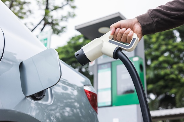 Ev car Coche eléctrico cargando en el estacionamiento. Mano masculina sosteniendo el cable de alimentación conectado a la estación de carga de automóviles eléctricos. Energía alternativa ecológica. Vehículo de batería de tecnología futura.