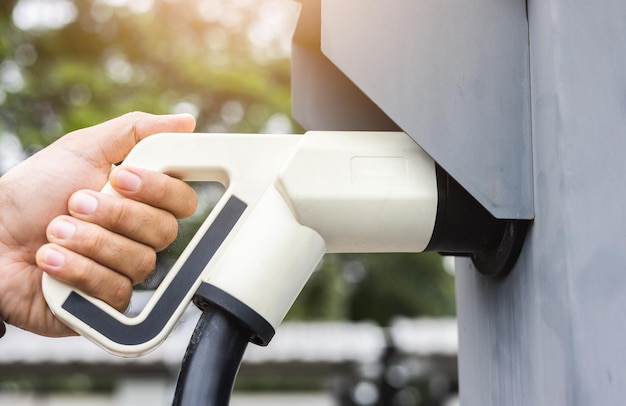 Ev car Coche eléctrico cargando en el estacionamiento. Mano masculina sosteniendo el cable de alimentación conectado a la estación de carga de automóviles eléctricos. Energía alternativa ecológica. Vehículo de batería de tecnología futura.