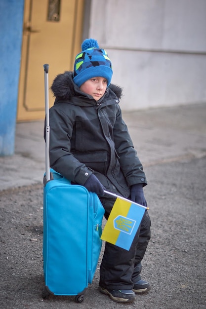 Evakuierung von Zivilisten Trauriges Kind mit der Flagge der Ukraine Flüchtlingsfamilie aus der Ukraine, die die Grenze überquert Hand mit einem Pass über dem Gepäck mit gelbblauer Flagge Stoppt die Kriegsunterstützung der Ukraine