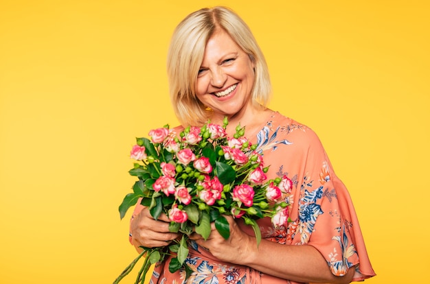 Evento festivo. Día de la Madre. Día de San Valentín. Cumpleaños. Retrato de mujer senior encantadora linda feliz en ropa colorida fiesta con gran ramo de flores sobre fondo amarillo