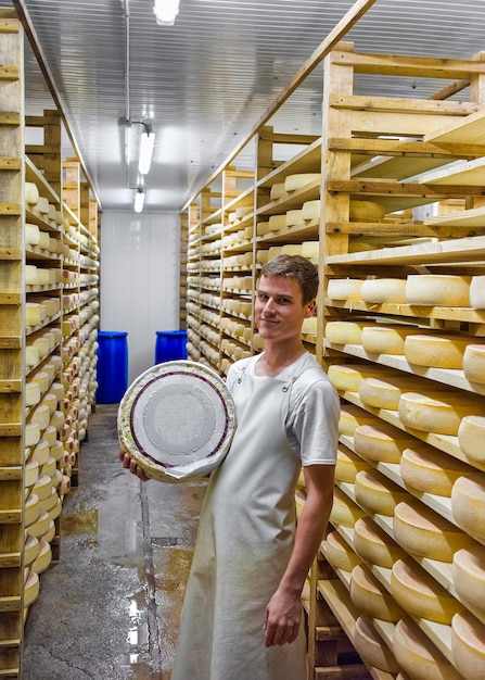 Evillers, Francia - 31 de agosto de 2016: Trabajador que sostiene la rueda del queso Gruyere de Comte en la bodega de maduración en la lechería Franche Comte en Francia