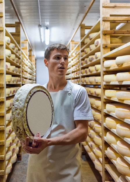 Evillers, Frankreich - 31. August 2016: Arbeiter, der ein Rad Gruyere de Comte-Käse im Reifekeller in der Molkerei Franche Comte in Frankreich hält