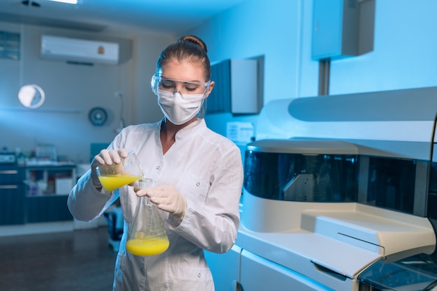 Foto exame de líquido químico amarelo. a menina analisa a substância nos frascos. um químico faz um teste rápido de um líquido amarelo.
