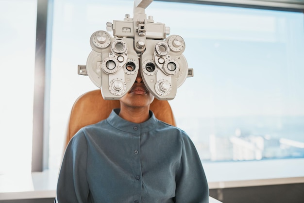 Exame oftalmológico de teste de optometria e mulher negra na clínica para teste de visão e avaliação óptica Consulta de optometrista de saúde e paciente com equipamento médico phoropter e lente para olhos