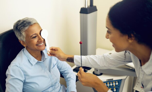 Foto exame oftalmológico feminino e oclusor com optometrista na clínica, verificação e lentes para bem-estar visual ou cuidados de saúde ferramentas de visão médica e sorriso para obter ajuda na consulta de avaliação ou cobertura no hospital