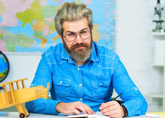 Examen en la universidad. Profesor trabajando en la mesa en el aula. Maestro de escuela primaria masculino en el aula.