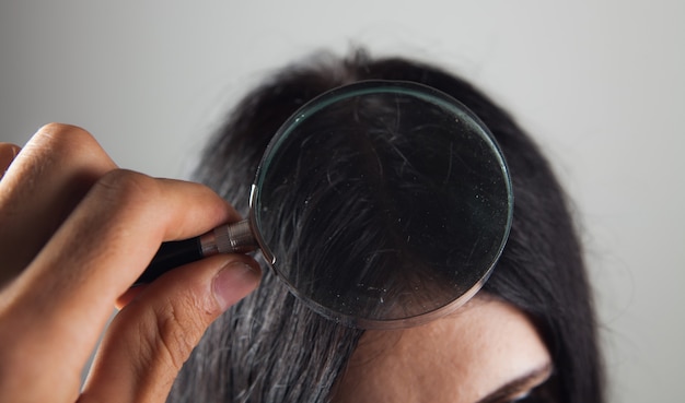 Examina el cabello de una mujer joven con una lupa.