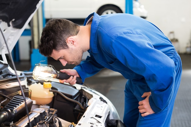 Examinação mecânica sob o capô do carro com tocha