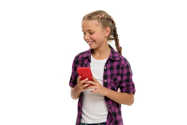 Examinando su dispositivo de teléfono de marca Dependencia del teléfono móvil Chica linda niña pequeña sonriendo a la pantalla del teléfono Navegación por Internet y redes sociales Adicción u obsesión por teléfono móvil e Internet