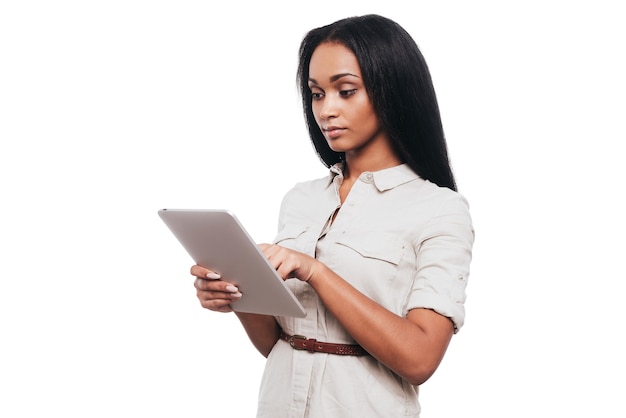 Examinando su nueva pestaña. Confianza joven africana trabajando en tableta digital mientras está de pie contra el fondo blanco.