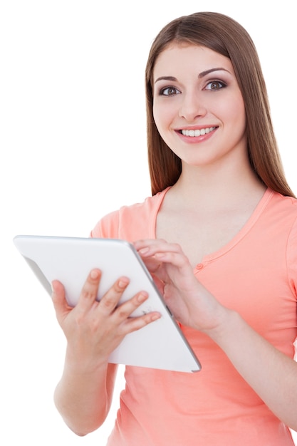 Examinando su nueva tableta digital. Atractiva mujer joven sosteniendo tableta digital y sonriendo mientras está de pie aislado en blanco