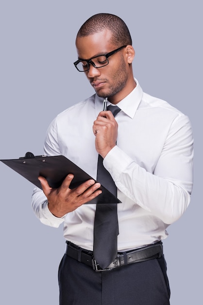 Foto examinar el contrato antes de firmarlo. hombre africano joven pensativo en camisa y corbata