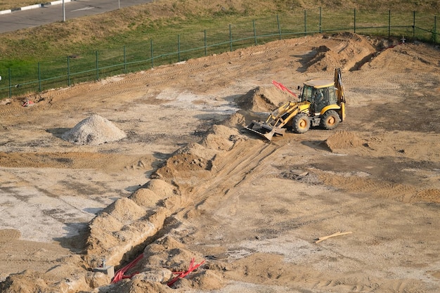 Excavadora amarilla cavando trincheras para cables y alambres en un sitio de construcción