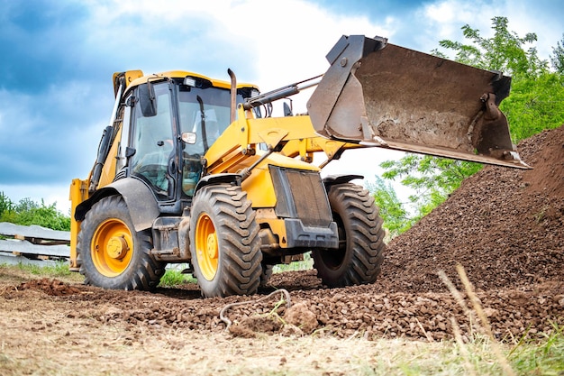 Una excavadora amarilla o un cargador está cavando activamente la tierra en un campo moviendo y desplazando el suelo para despejar el área para la construcción o fines agrícolas