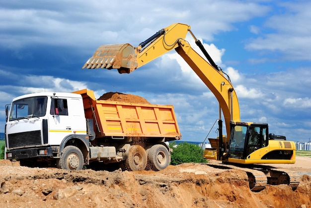 Excavadora cargando un camión de descarga en un pozo de arena sobre el cielo azul