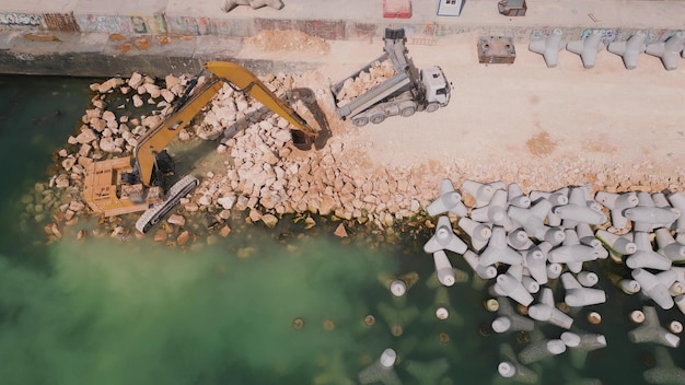 Una excavadora construye diligentemente un muelle o rompeolas en el mar, su poderoso brazo se extiende desde la orilla creando una estructura resistente en medio de las olas Vista aérea