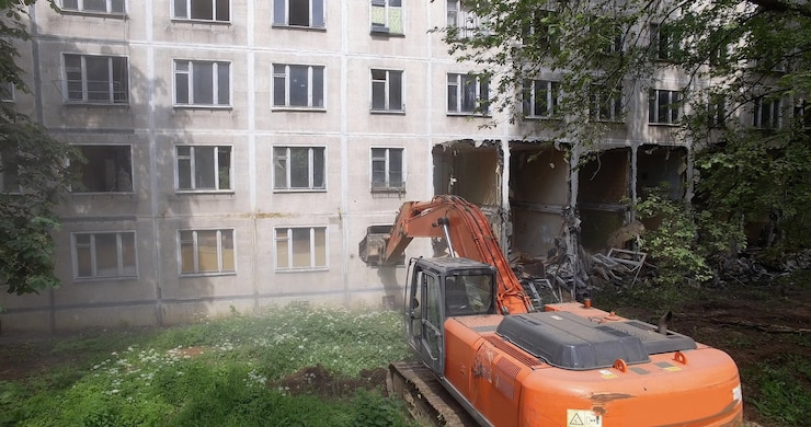 Una excavadora destruye la pared exterior de un edificio residencial con su cucharón