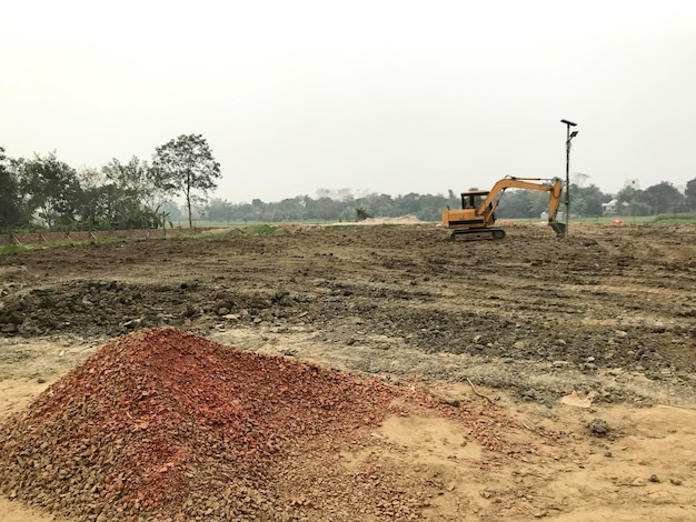 Una excavadora está en el campo frente a un árbol.