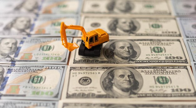 La excavadora de juguete amarilla extrae minerales en forma de billetes de dólar