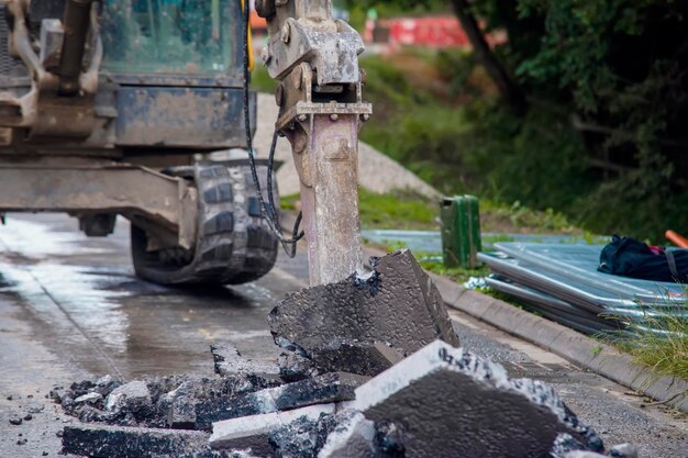 Excavadora con martillo hidráulico rompiendo asfalto en preparación para obras de drenaje