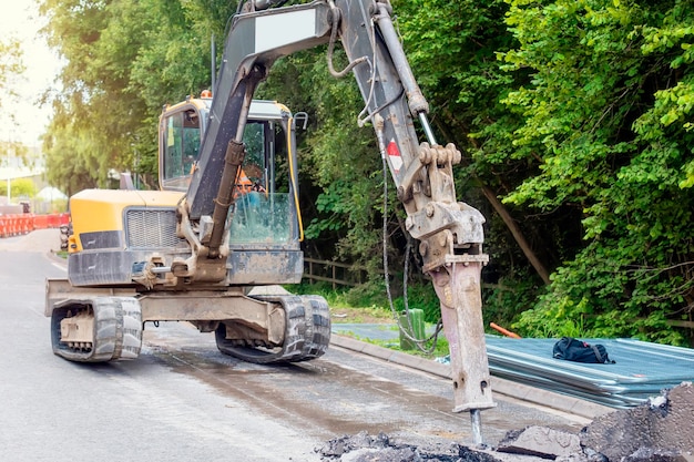 Foto excavadora con martillo hidráulico rompiendo asfalto en preparación para obras de drenaje