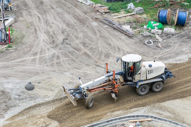 Una excavadora nivela y compacta la arena antes de colocar el asfalto en un sitio de construcción