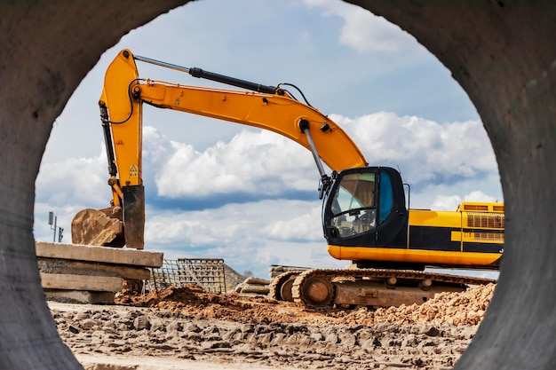 Excavadora pesada en el sitio de construcción Vista de la excavadora a través de la tubería de hierro Equipos de construcción para movimiento de tierras Excavadora de cantera