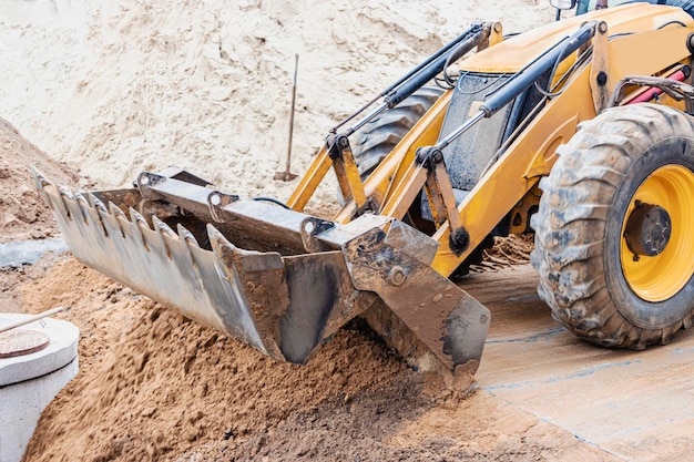 La excavadora rellena el pozo con el cucharón delantero. Mueve el suelo alrededor del sitio de construcción. De cerca. Equipo pesado de construcción.