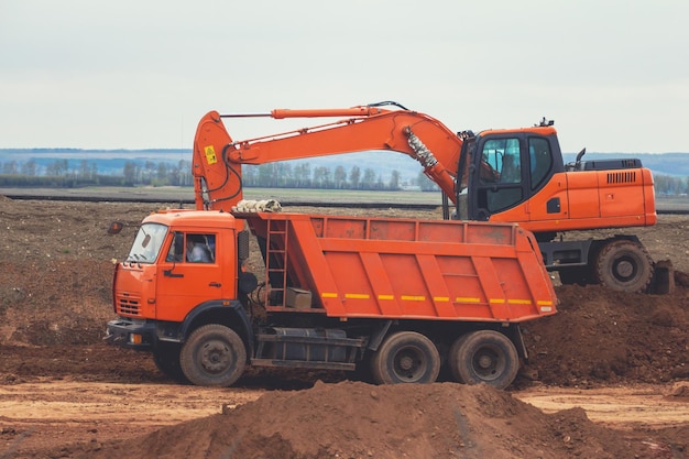 Excavadora roja cargando el camión volquete en la construcción de la carretera, telefoto