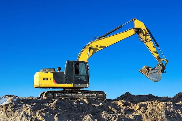 Excavadora trabaja sobre el terreno en el cielo azul de fondo.