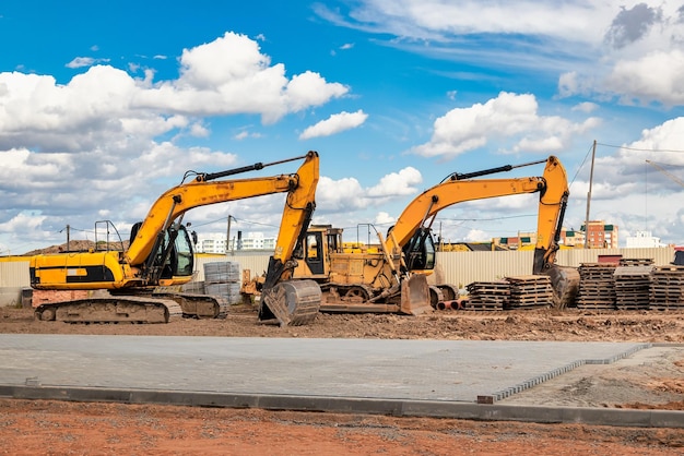 Excavadoras potentes en un sitio de construcción contra un cielo azul nublado Equipos de construcción de movimiento de tierras Muchas excavadoras