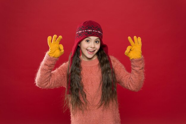 Excelente clima. traje de invierno Linda modelo disfruta del estilo invernal. El niño pequeño usa gorro de punto. Mantente caliente. Accesorio de moda de invierno para niña pequeña. Niño pequeño cabello largo usar sombrero burdeos fondo.