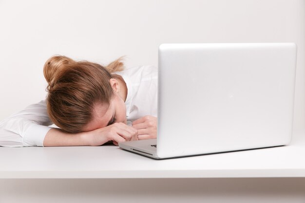 Excesso de trabalho e cansada dormindo em um laptop em uma mesa de trabalho em seu escritório