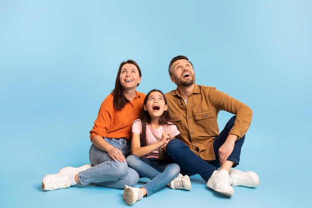 Foto excitada familia de padres e hija mirando hacia arriba sentado en el estudio