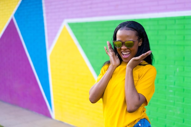 Excitada y feliz chica africana gritando junto a una pared colorida