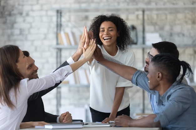 Excitada mulher de negócios afro-americana de sucesso com empresários multirraciais dando high five celebrando a vitória Equipe de funcionários felizes envolvidos em atividade de construção de equipe em reunião corporativa