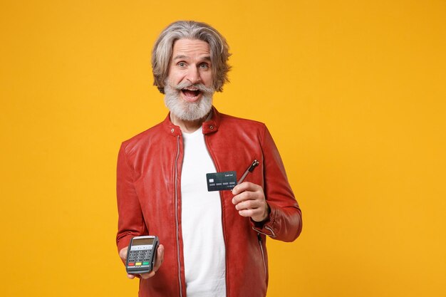 Foto excitado anciano de pelo gris bigote barbudo hombre aislado sobre fondo amarillo. concepto de estilo de vida de las personas. simulacros de espacio de copia. mantenga un terminal de pago bancario moderno para procesar pagos con tarjeta de crédito.