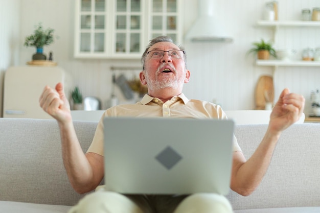 Excitado homem idoso de meia-idade eufórico vencedor avô mais velho maduro olhando para o laptop lendo
